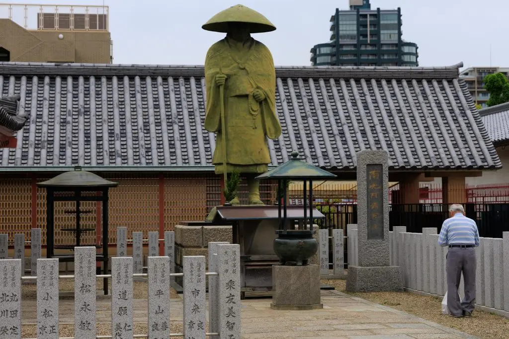 Paying respects to Kobo Daishi (Kukai). The inscription Namu Daishi Henjo Kongo on the stone pillar marks this as a site of Shingon Buddhism
